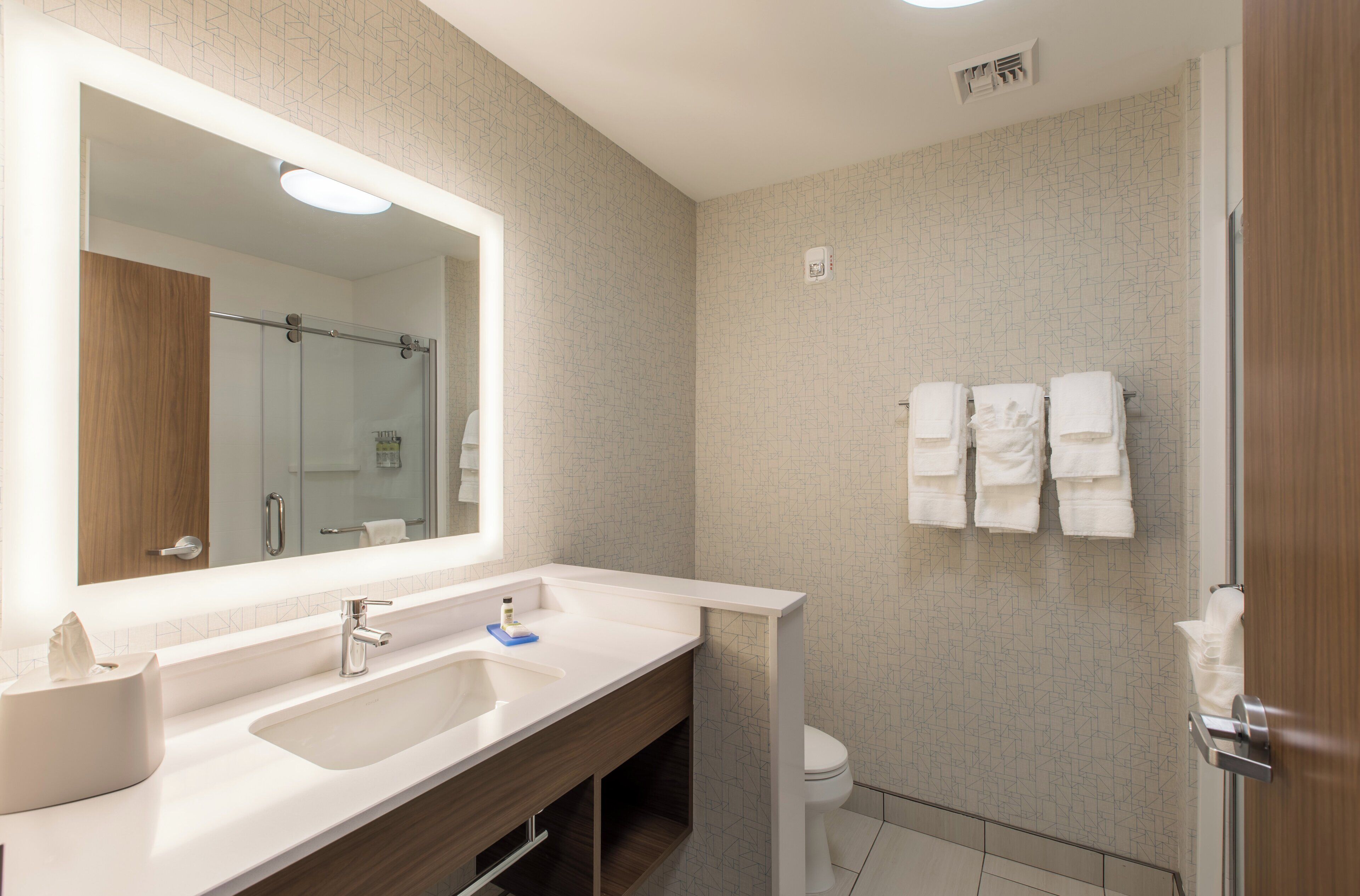 A modern bathroom with a large mirror, two sinks, a toilet, and a shower area.