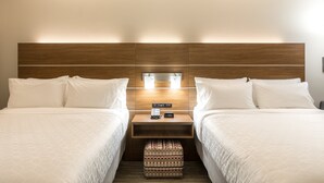 A hotel room with two beds, a wooden headboard, bedside lamps, a nightstand with a phone and a clock, and a patterned ottoman. - Holiday Inn Express & Suites Greenville S- Piedmont by IHG (Piedmont)