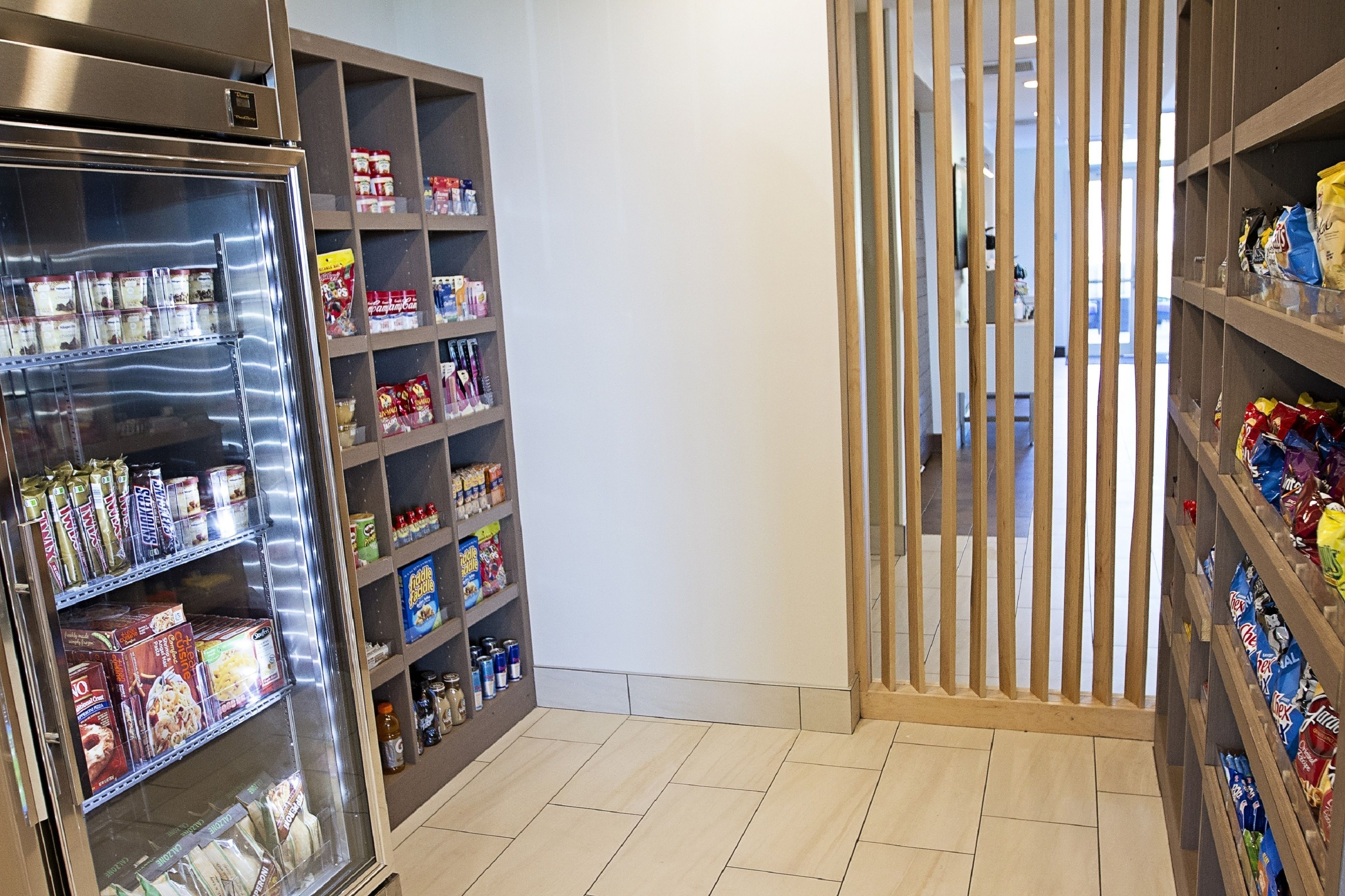 Un expositor refrigerado con alimentos envaselados y una estantería de madera con aperitivos.