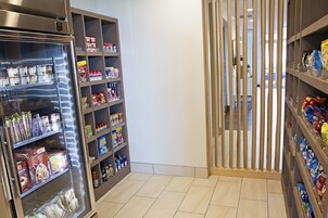 Un expositor refrigerado con alimentos envaselados y una estantería de madera con aperitivos.