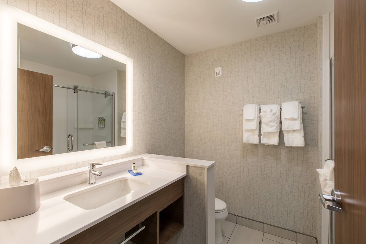 A modern bathroom with a large mirror, two sinks, a toilet, and a shower area.