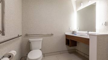 A modern bathroom with a toilet, handrail, sink, mirror, and toilet paper.