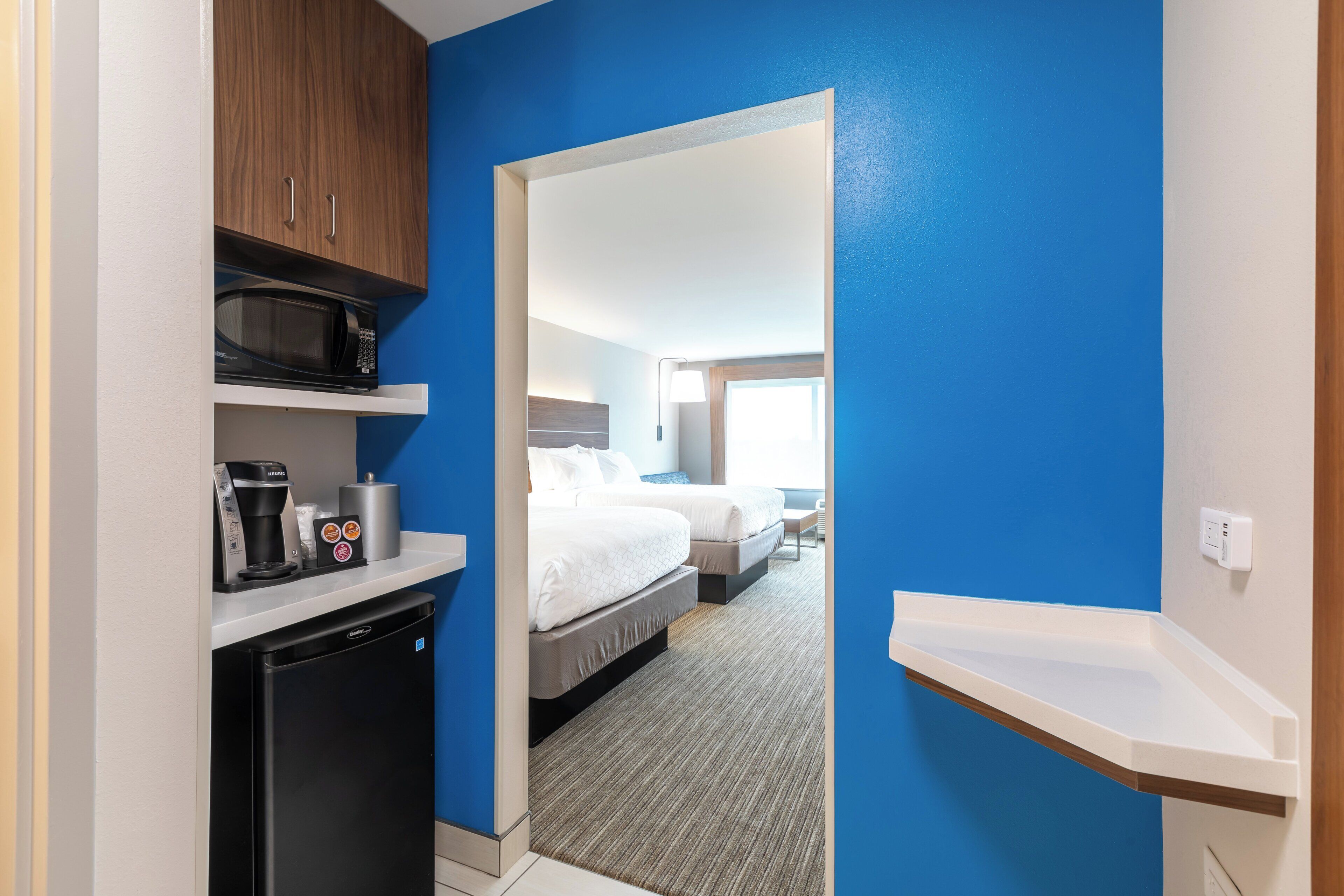 A compact hotel room with a kitchenette, a bed, and a bathroom.
