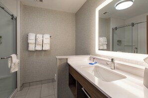 A modern bathroom with a glass shower enclosure, a white sink with a mirror, and towels hanging on a rack.