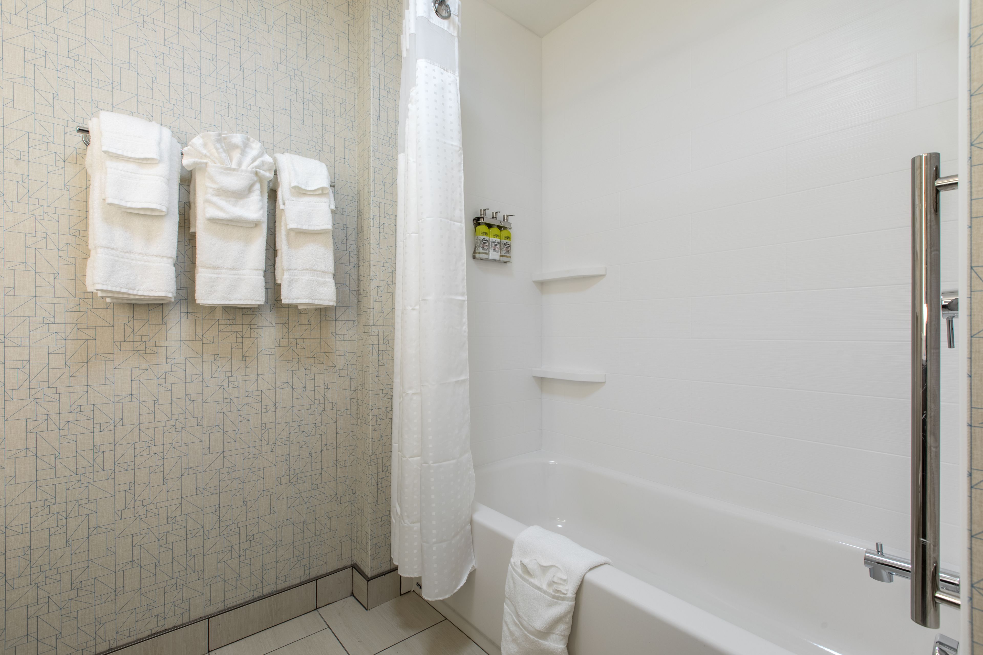 Een badkamer met een douche, een bad en drie handdoeken die aan de muur hangen.