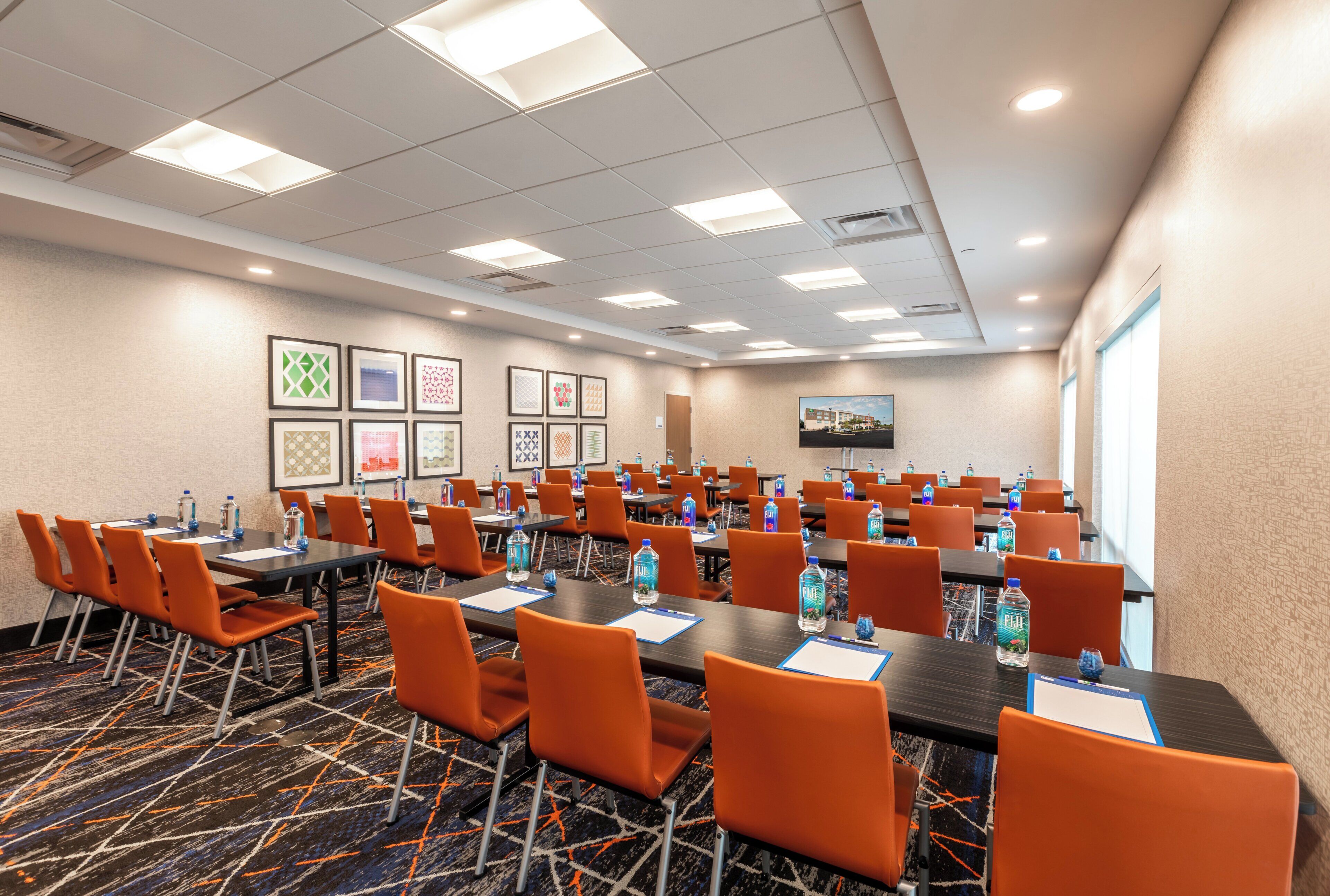 A conference room with multiple tables and chairs, water bottles, and framed artwork on the walls.
