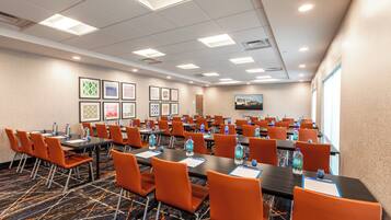 A conference room with multiple tables and chairs, water bottles, and framed artwork on the walls.