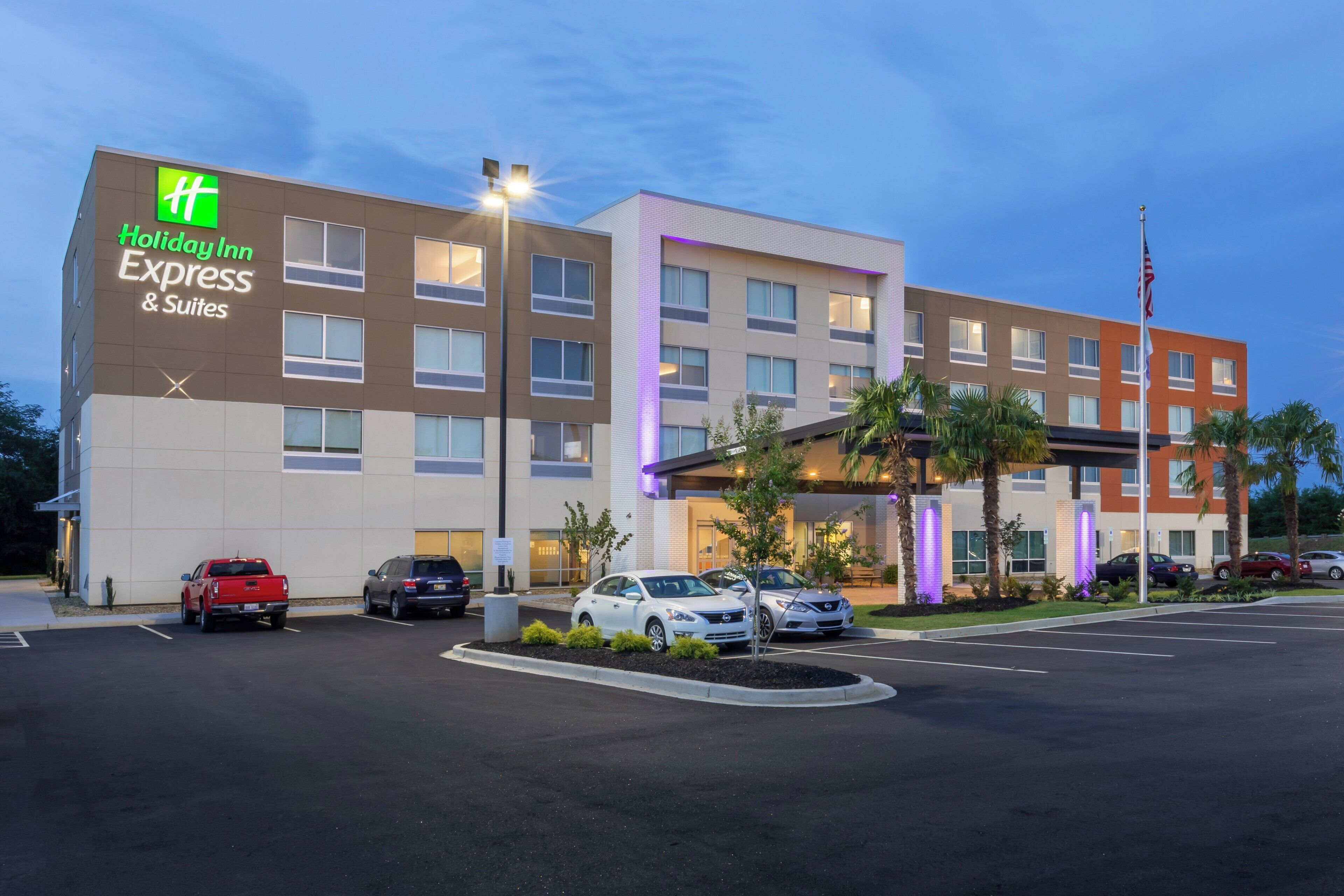 Een Holiday Inn Express & Suites hotel met een parkeerplaats en verschillende geparkeerde auto's voor het gebouw.