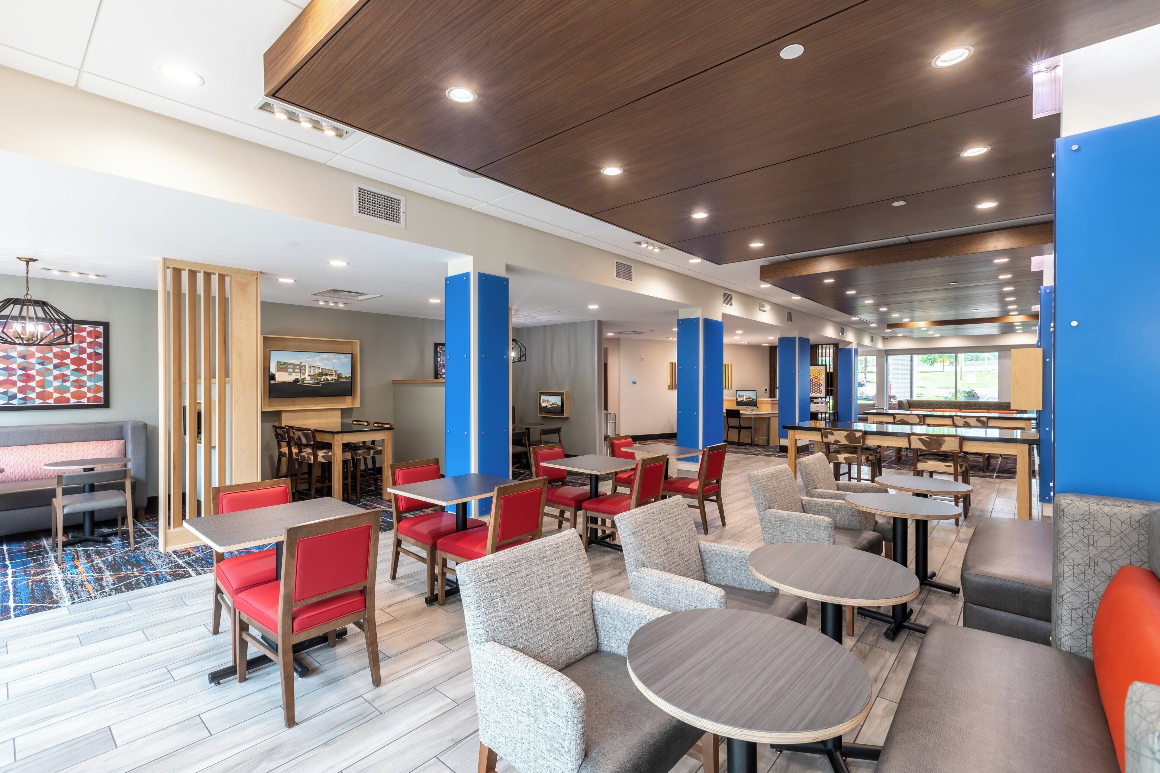 A hotel lobby with multiple seating areas, including tables and chairs, a reception desk, and a large screen displaying a cityscape.