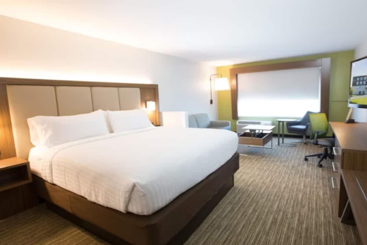 A hotel room with a large bed, a desk, a chair, and a small table.