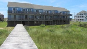 Ein mehrgeschossiges Gebäude direkt am Strand mit einer Holzterrasse, die zum Eingang führt.