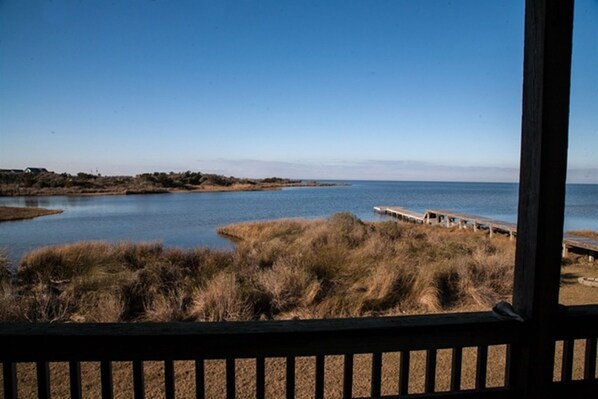 A view of a calm body of water with a wooden pier extending into it, surrounded by grassy areas. - Sw 4 Seas-the-day 1 Bedroom Condo by RedAwning (Hatteras)