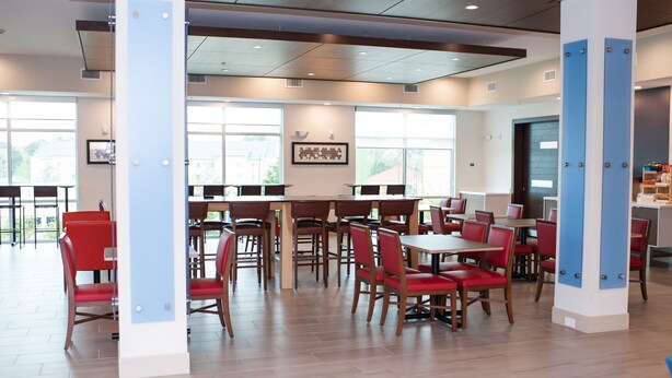 A modern dining area with wooden tables and red chairs, large windows, and a clean, bright atmosphere.