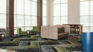 A modern lobby with large windows, a patterned carpet, and a seating area with a sofa and chairs.