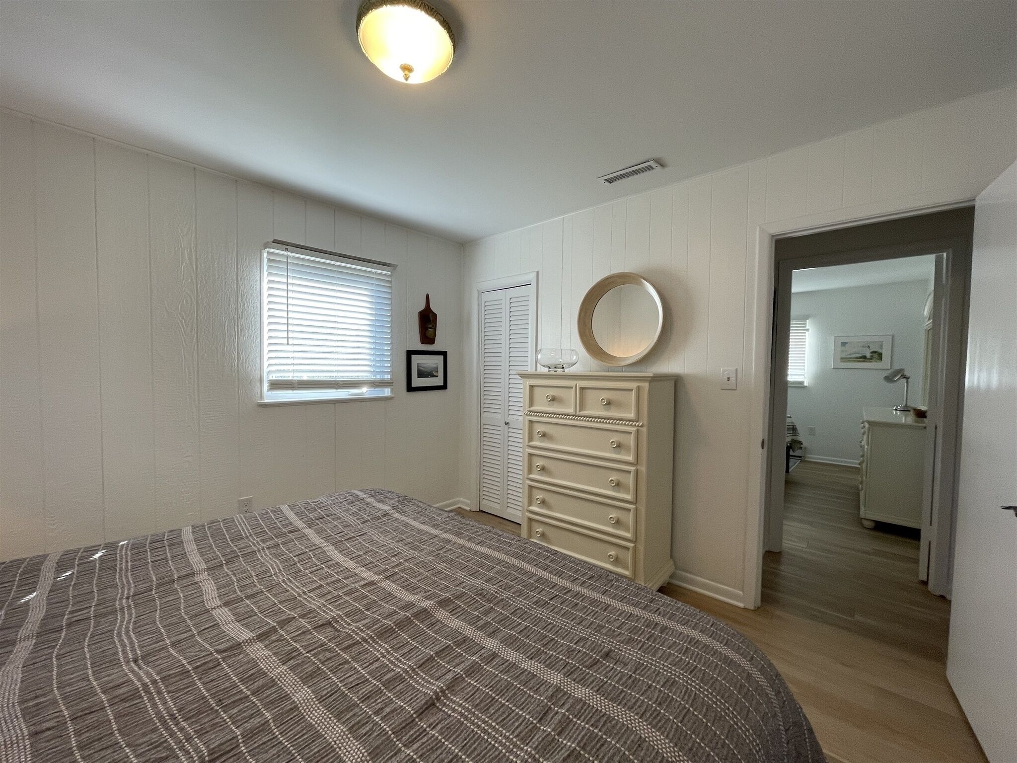 Ein Schlafzimmer mit Bett, Kommode und einem Fenster mit Jalousien.
