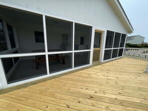 A covered deck with a wooden floor, large windows, and a white railing. - 58223 Dunes Dr House by RedAwning (Hatteras)