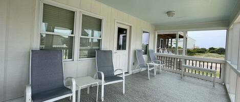A covered porch with white chairs and a table, a door, and a view of the outside.