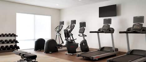 Un gimnasio con cintas de correr, elípticas y una banca.