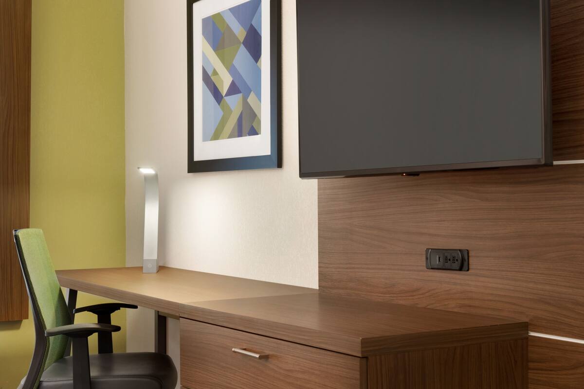 A modern office space with a wooden desk, a green chair, a framed abstract painting, and a flat-screen TV mounted on a wooden wall.