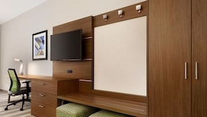 A modern office space with a wooden desk, a flat-screen TV, a framed picture, and a green patterned ottoman. - Holiday Inn Express & Suites-Cincinnati South - Wilder by IHG (Newport)
