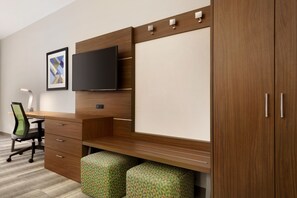 Un espace de bureau moderne avec un bureau en bois, un téléviseur à écran plat, un tableau encadré et un pouf vert à motifs.