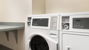 A row of white front-loading washing machines with control panels, including operating and dispenser instructions. - Holiday Inn Express & Suites-Cincinnati South - Wilder by IHG (Newport)