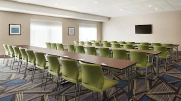 Un salón de conferencias con una larga mesa, varias sillas, cuadros en las paredes y un televisor de pantalla plana.