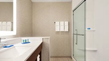 A modern bathroom with a glass shower enclosure, a white sink with a mirror, and a towel rack with white towels.