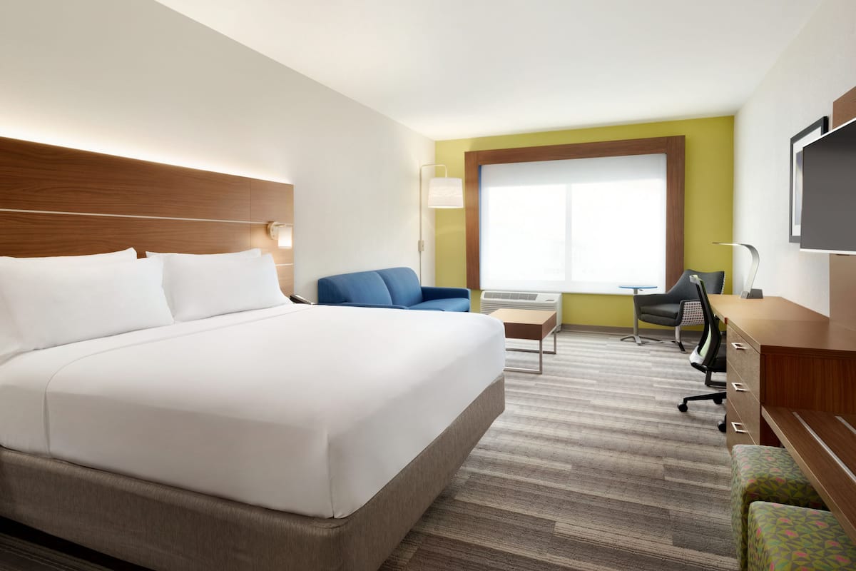 A hotel room with a large bed, a desk, a chair, and a TV.
