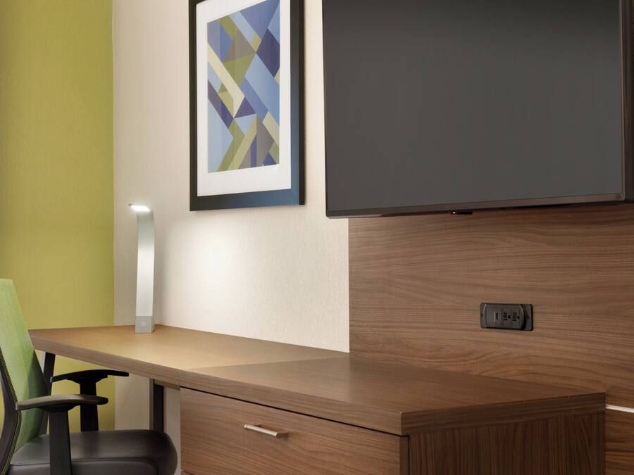 Een moderne kantoorruimte met een houten bureau, een groene stoel, een lijst met abstracte kunst en een flatscreenmonitor.