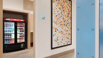 Un pasillo con una máquina expendedora, una obra de arte geométrica enmarcada y una puerta azul.