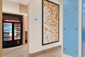 A hallway with a vending machine, a framed geometric artwork, and a blue door. - Holiday Inn Express & Suites-Cincinnati South - Wilder by IHG (Newport)