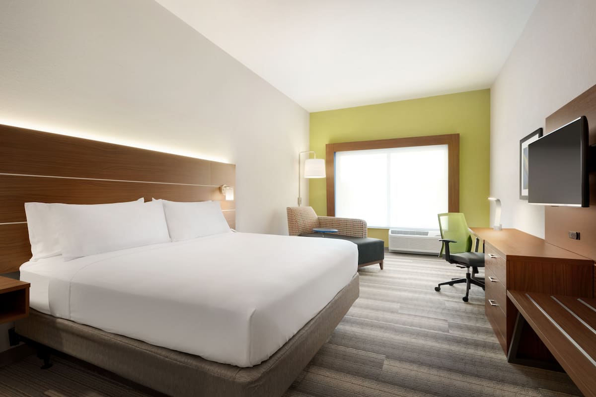 A hotel room with a large bed, a desk, a chair, and a TV.