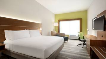 A hotel room with a large bed, a desk, a chair, and a TV.