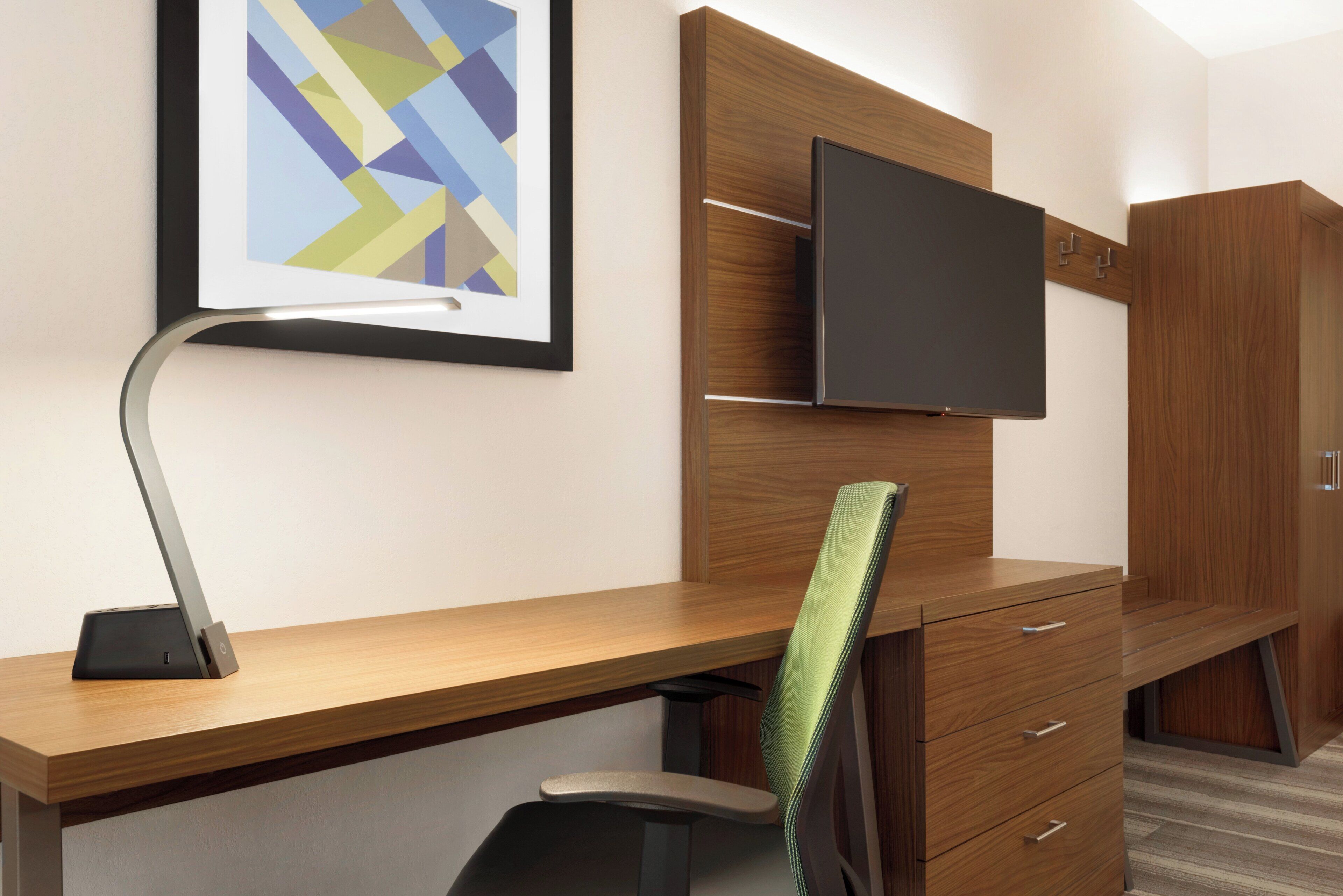 Habitación de hotel con un escritorio de madera, una silla, un televisor de pantalla plana montado en la pared y un cuadro enmarcado sobre el escritorio.