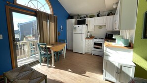 A compact kitchen with white cabinets, a stove, and a refrigerator. There is a dining area with a table and chairs.