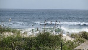A beach with waves, vegetation, and a wooden fence.