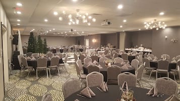 A banquet hall with round tables, chairs, and a Christmas tree.