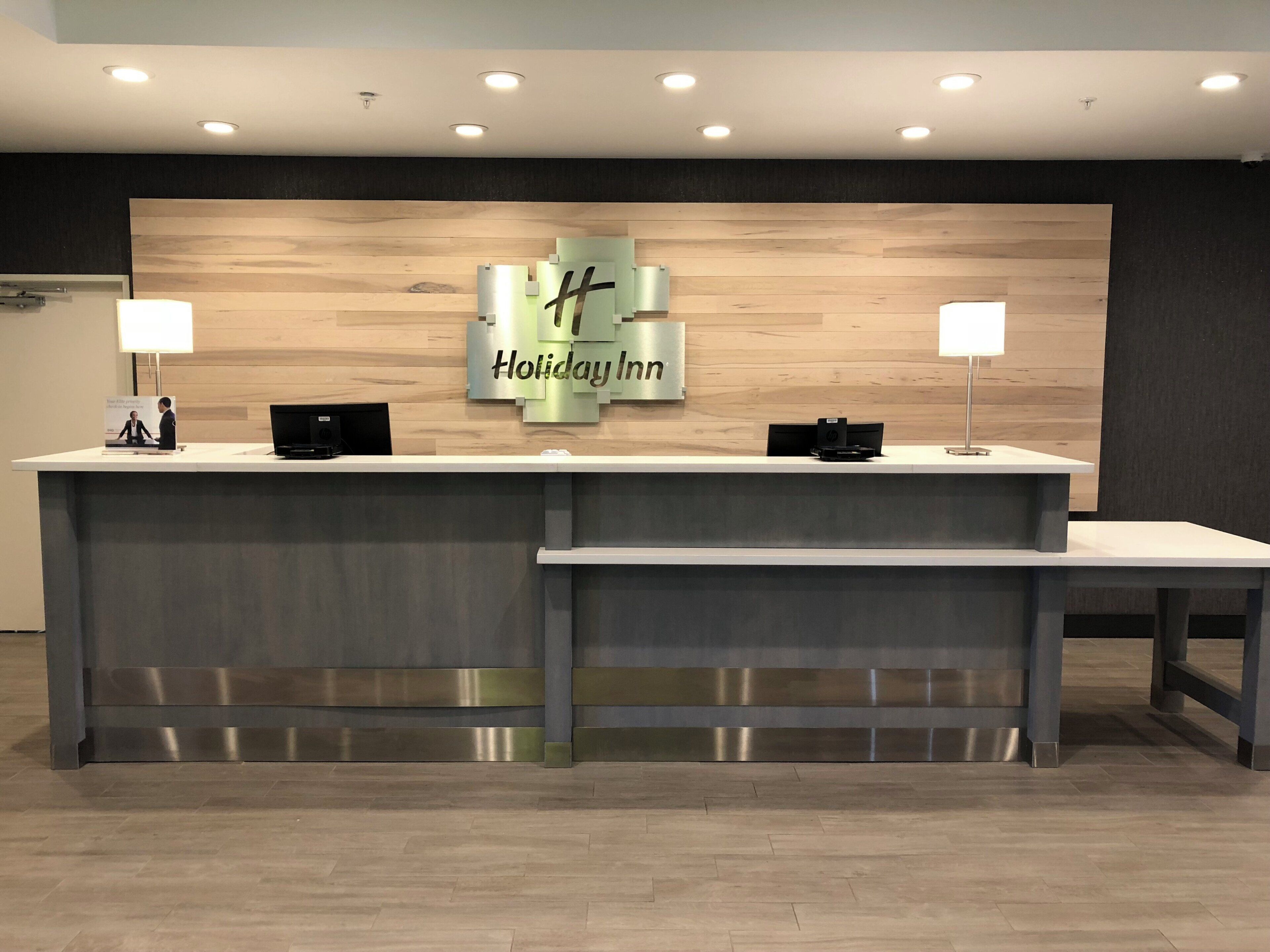 A reception desk with a 'Holiday Inn' sign, two computer monitors, and a modern design.