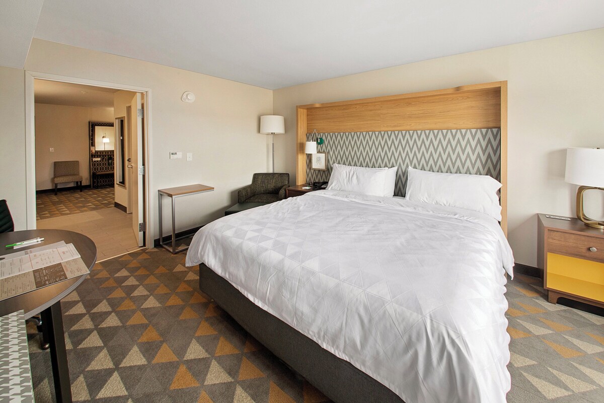 Une chambre d’hôtel avec un grand lit, un bureau, une chaise et une table de chevet avec une lampe.