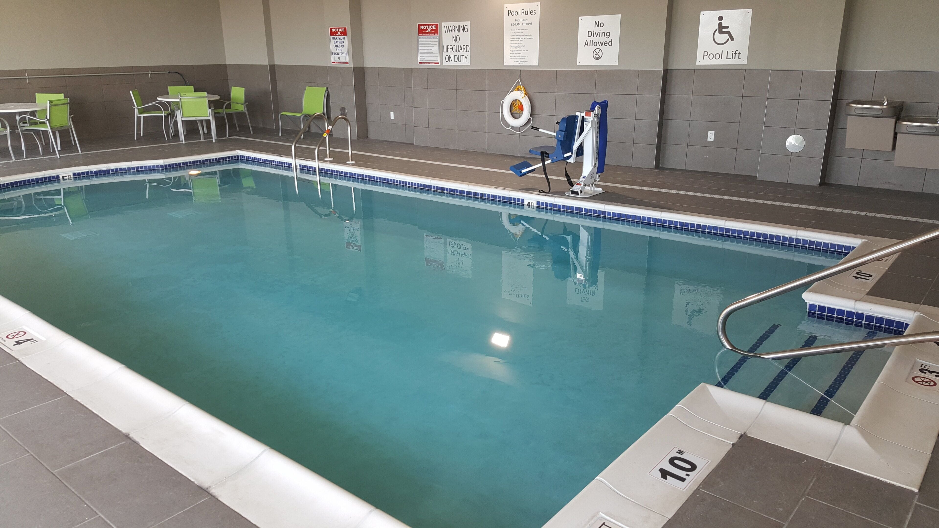 An indoor swimming pool with clear water, a lifeguard stand, and poolside chairs.