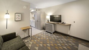 A hotel room with a sofa, a TV, a desk, and a patterned carpet.