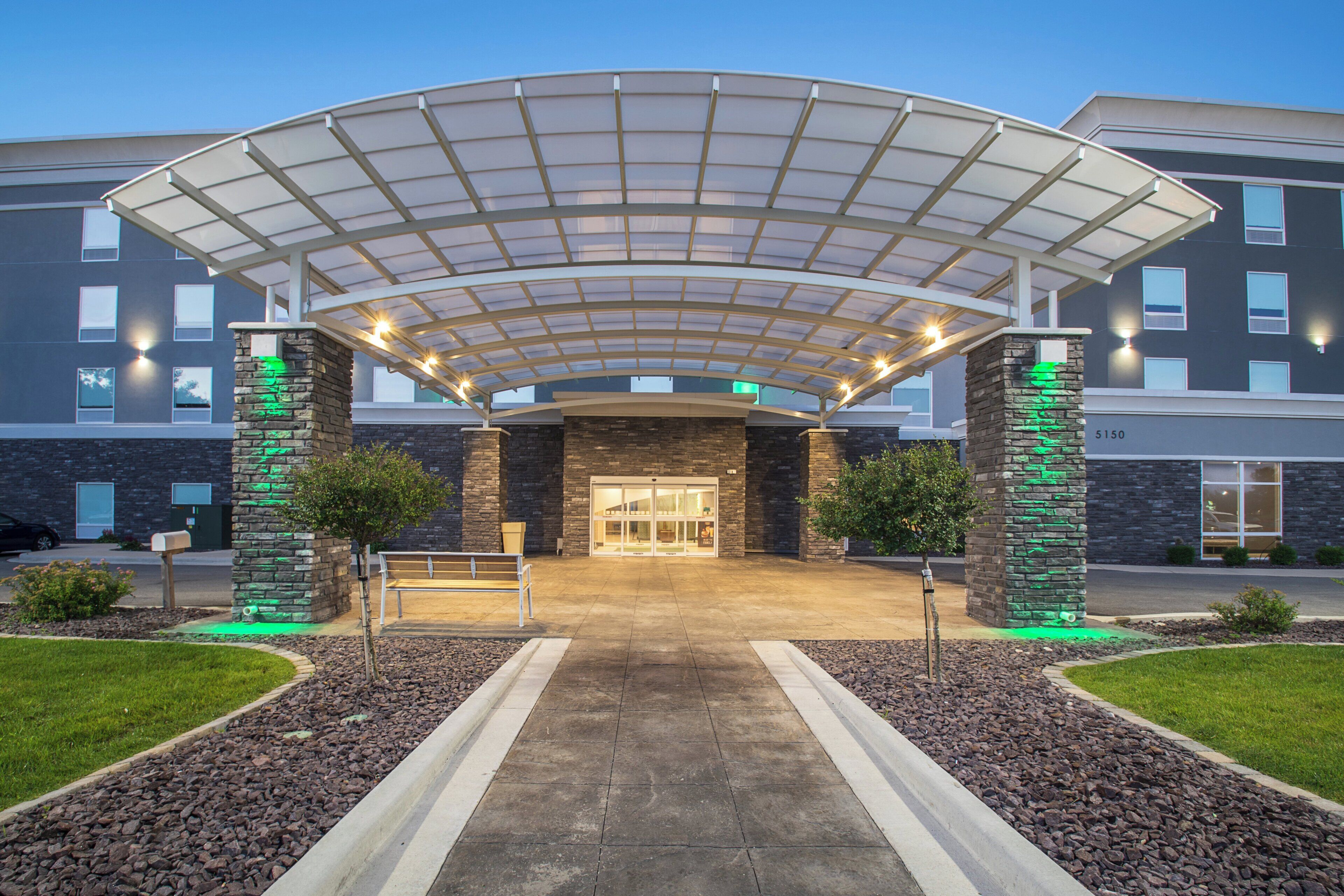 A hotel entrance with a covered walkway, stone pillars, and a well-maintained lawn.