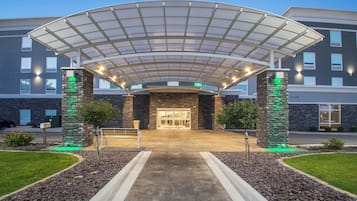 A hotel entrance with a covered walkway, stone pillars, and a well-maintained lawn.