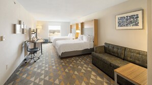 A hotel room with two beds, a desk, a couch, and a large window.