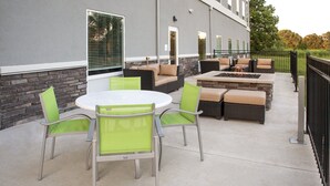 An outdoor patio with a round table and chairs, a fire pit, and a seating area with cushions.