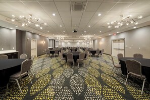 Ein Konferenzraum mit mehreren Tischen und Stühlen, einem gemusterten Teppich und Deckenleuchten.