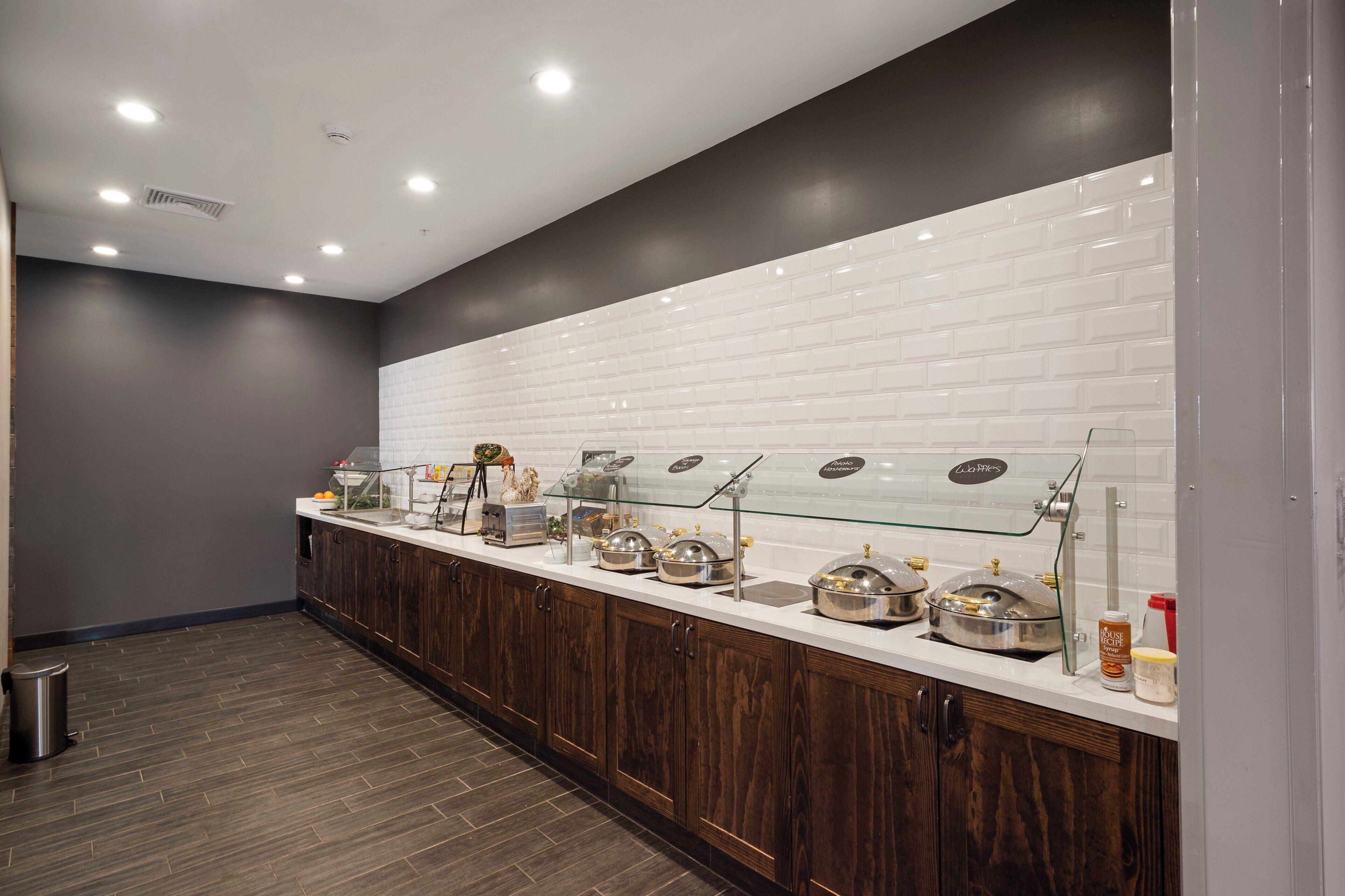 Zona de bufé con salpicadero blanco de azulejos, armarios de madera y vitrina de vidrio.