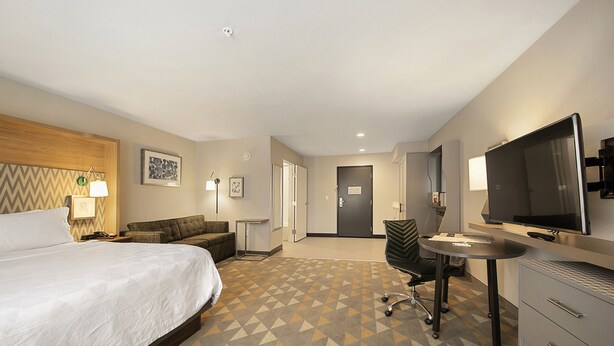A hotel room with a bed, a desk, a chair, a television, and a filing cabinet.