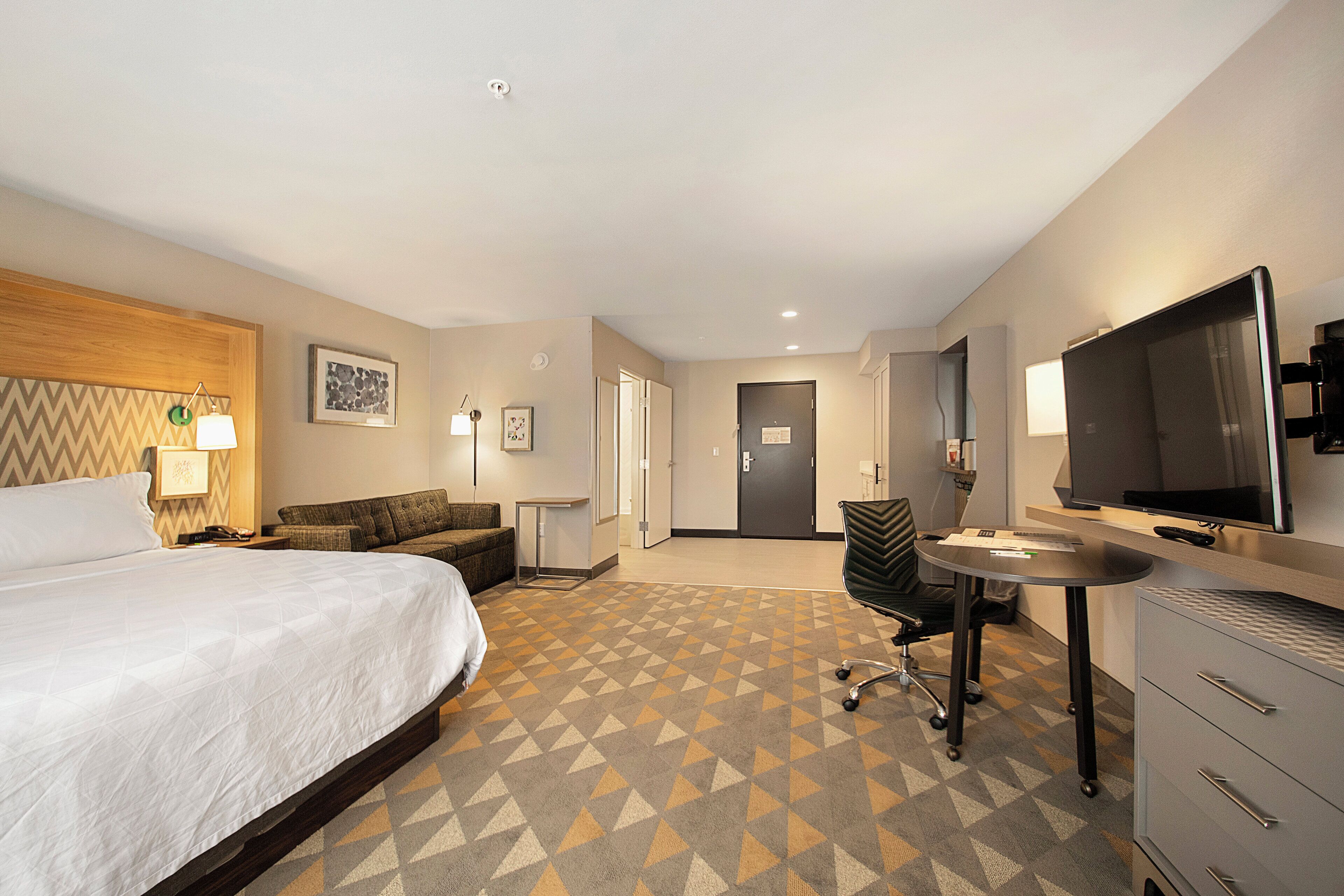 A hotel room with a bed, a desk, a chair, a television, and a wardrobe.